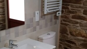 A bathroom with a white sink, wooden vanity, a white toilet, and a stone wall. - Apartment 'Arriba' with Shared Terrace, Balcony and Wi-Fi (Afonsagrada)