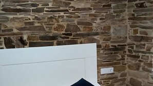 A bedroom with a stone wall, a white headboard, and a patterned bedspread. - Apartment 'Arriba' with Shared Terrace, Balcony and Wi-Fi (Afonsagrada)