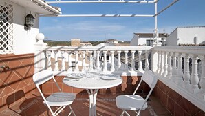 Eine Terrasse mit einem weißen Tisch und Stühlen, einem weißen Geländer und Blick auf die Stadt.