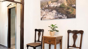 Ein Flur mit einem Holzstuhl, einem kleinen Tisch mit einer Pflanze und einem gerahmten Bild einer Stadt an der Wand.