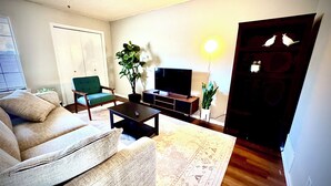 Een woonkamer met een bank, een salontafel, een televisie op een dressoir en twee planten in potten.