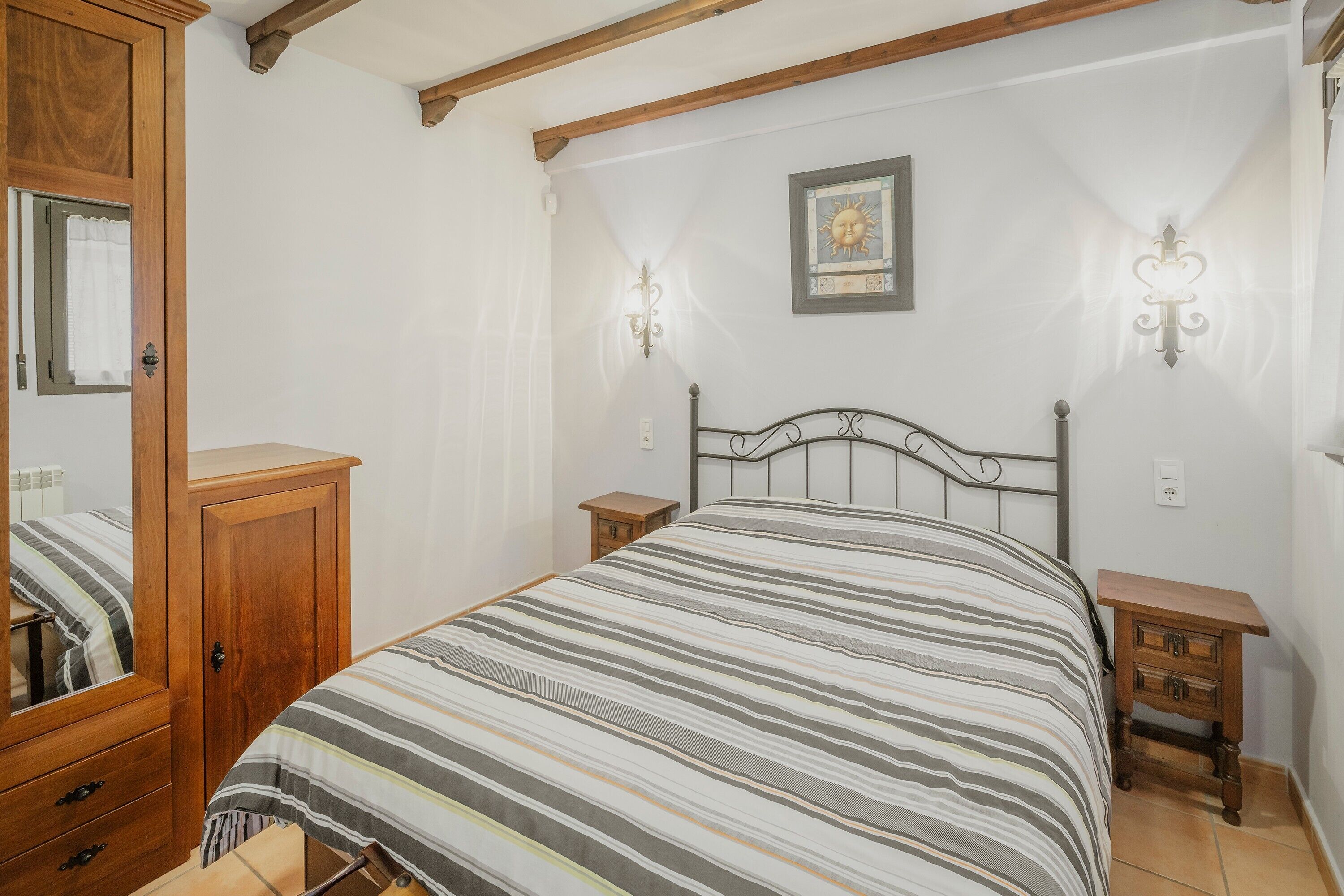 Een slaapkamer met een bed, een houten garderobe, twee nachtkastjes en een wandlamp.