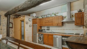 A kitchen with wooden cabinets, a washing machine, a microwave, and a dining area with a bench.