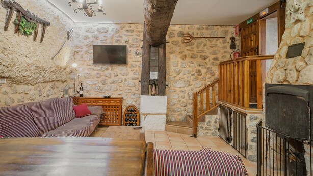 A rustic interior with stone walls, a wooden staircase, a fireplace, and a sofa.