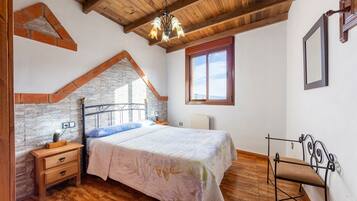 A bedroom with a bed, nightstand, chair, wooden ceiling, brick wall, and a window.