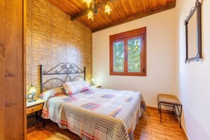 Un dormitorio con cama, mesita de noche, lámpara, ventana y un taburete.