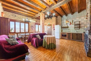 A cozy room with a wooden ceiling, a dining table, a sofa, and a kitchen area with a refrigerator and tiled backsplash.