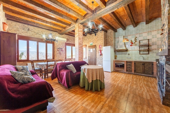 Una habitación acogedora con techo de madera, una mesa de comedor, un sofá y una zona de cocina con refrigerador y salpicadero de azulejos.