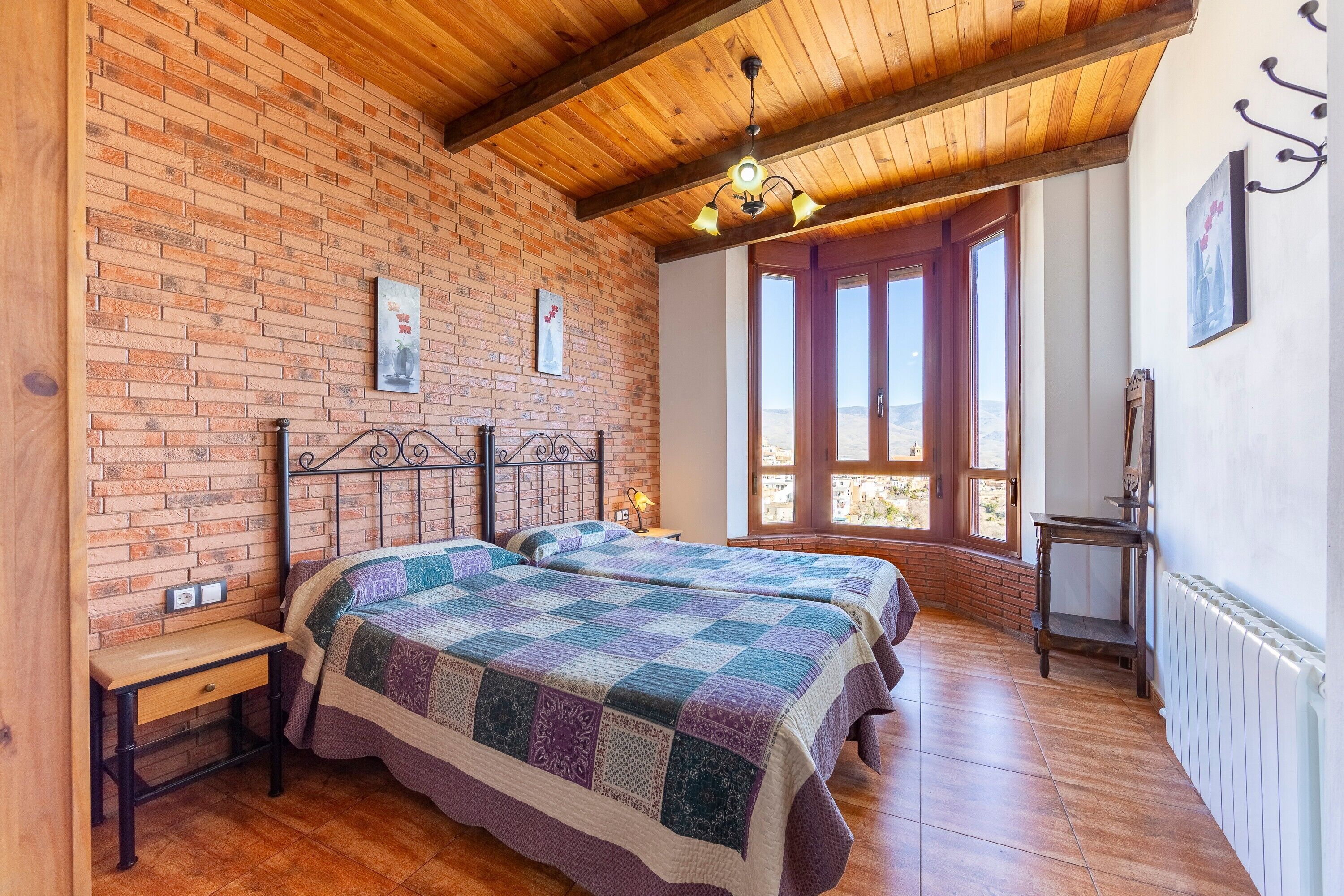 Een kamer met twee bedden, een houten plafond, bakstenen muren en een raam met uitzicht.