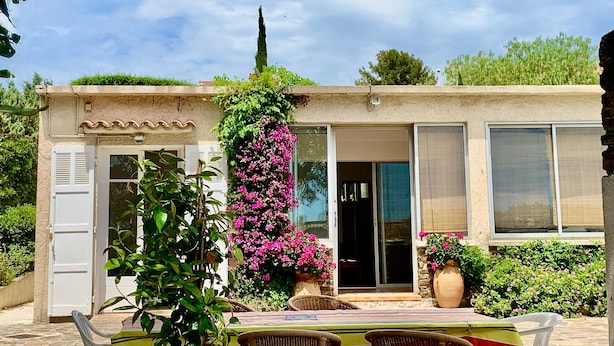 Un bâtiment doté d’un jardin, d’une pergola ornée de fleurs et d’une terrasse avec des chaises.