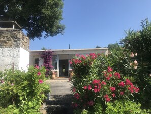 Un bâtiment doté d’une façade en pierre, d’un mur blanc et d’un jardin où poussent des fleurs roses.
