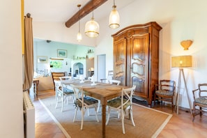 A dining area with a wooden table, white chairs, and hanging pendant lights. - Holiday Home “Mas Lis Amélie” with Mountain View, Wi-Fi and Air Conditioning (Eygalières)