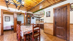 A dining area with a wooden table and chairs, a kitchen in the background, and a wooden door. - Casa Rural La Jirola - La Vivienda 1 with Mountain Views, Wi-Fi, and Air Conditioning (Abrucena)