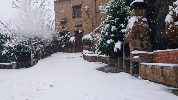 A snow-covered courtyard with a stone building, a wooden fence, and snow-laden trees. - Casa Rural La Jirola - La Vivienda 1 with Mountain Views, Wi-Fi, and Air Conditioning (Abrucena)
