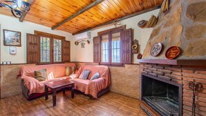 A cozy room with a stone wall, wooden ceiling, a fireplace, and a sofa with cushions. - Casa Rural La Jirola - La Vivienda 1 with Mountain Views, Wi-Fi, and Air Conditioning (Abrucena)