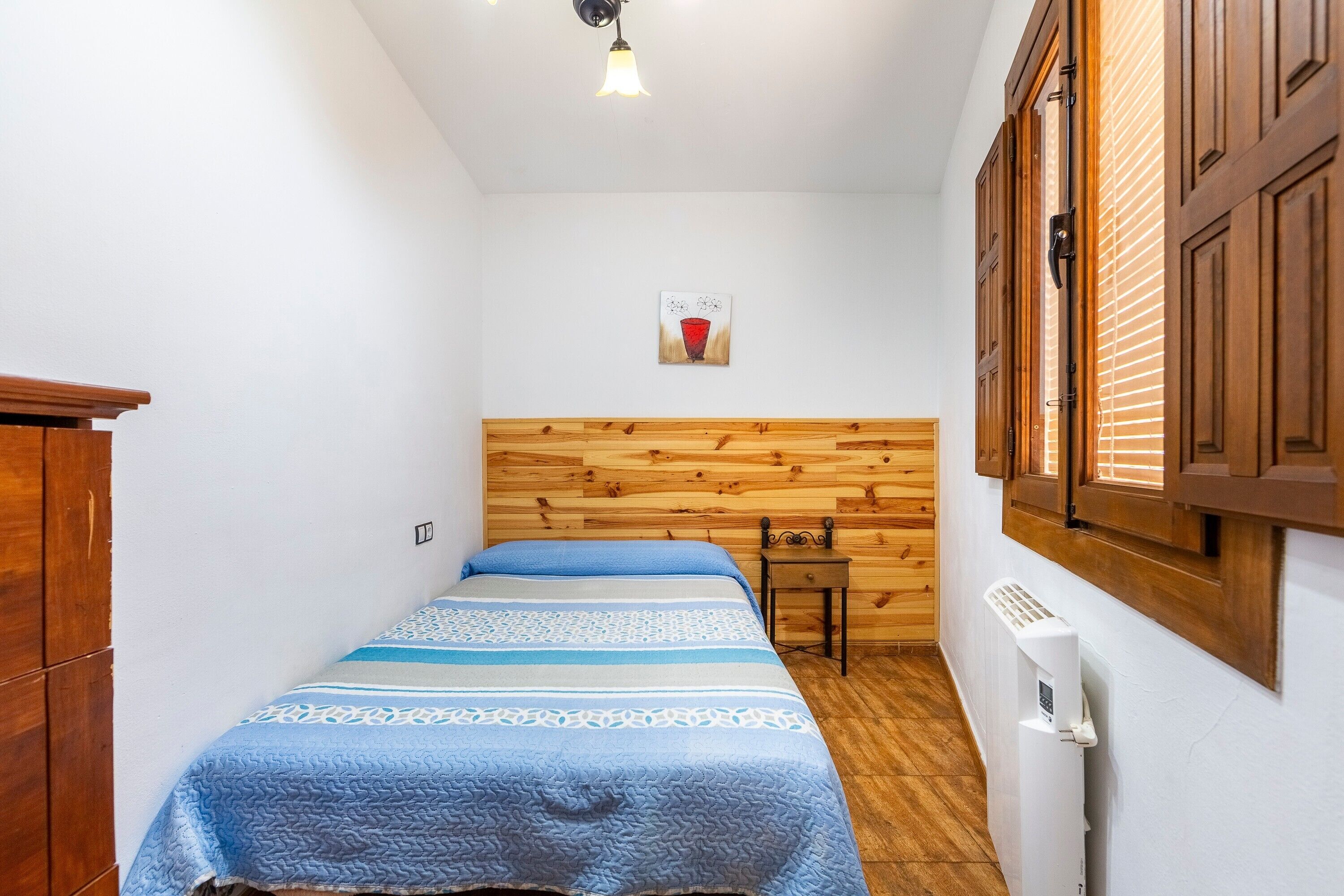Una habitación pequeña y acogedora con cabecera de madera, cama con colcha azul, una mesita y un radiador.