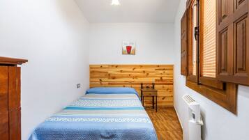 Una habitación pequeña y acogedora con cabecera de madera, cama con colcha azul, una mesita y un radiador.