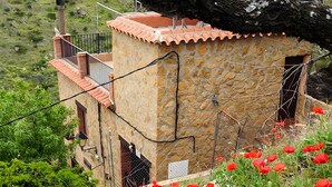 A stone building with a red-tiled roof, surrounded by a stone wall and a garden with red poppies. - Casa Rural La Jirola -Vivienda 2 with Mountain Views, Wi-Fi, and Air Conditioning (Abrucena)