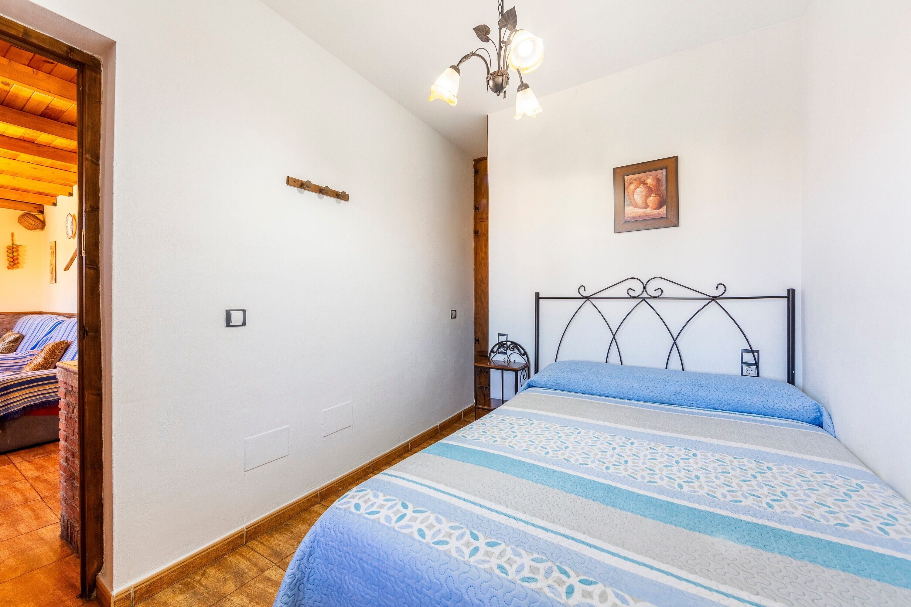 A bedroom with a bed, a bedside table, a wall-mounted picture, and a wooden door leading to another room.