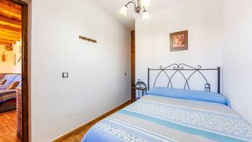 A bedroom with a bed, a bedside table, a wall-mounted picture, and a wooden door leading to another room.