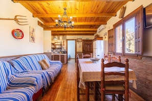 Una habitación acogedora con techo de madera, una mesa de comedor con sillas, un sofá y una zona de cocina al fondo.