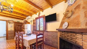A dining area with wooden chairs and a table, a fireplace, a television, and a kitchen with a refrigerator. - Casa Rural La Jirola -Vivienda 2 with Mountain Views, Wi-Fi, and Air Conditioning (Abrucena)