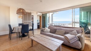 Ein modernes Wohnzimmer mit Sofa, Esstisch und Stühlen, einem Holztisch und einem großen Fenster mit Aussicht.