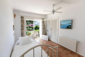 Quarto com cama, ventoinha no teto, vista para o jardim e um quadro na parede.