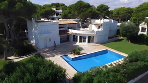 Una villa moderna con piscina, un porche cubierto y abundante vegetación.