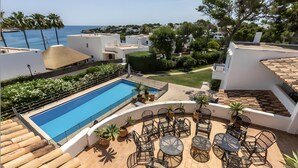 Una piscina en la azotea con vistas despejadas al mar, rodeada de mobiliario exterior y vegetación.