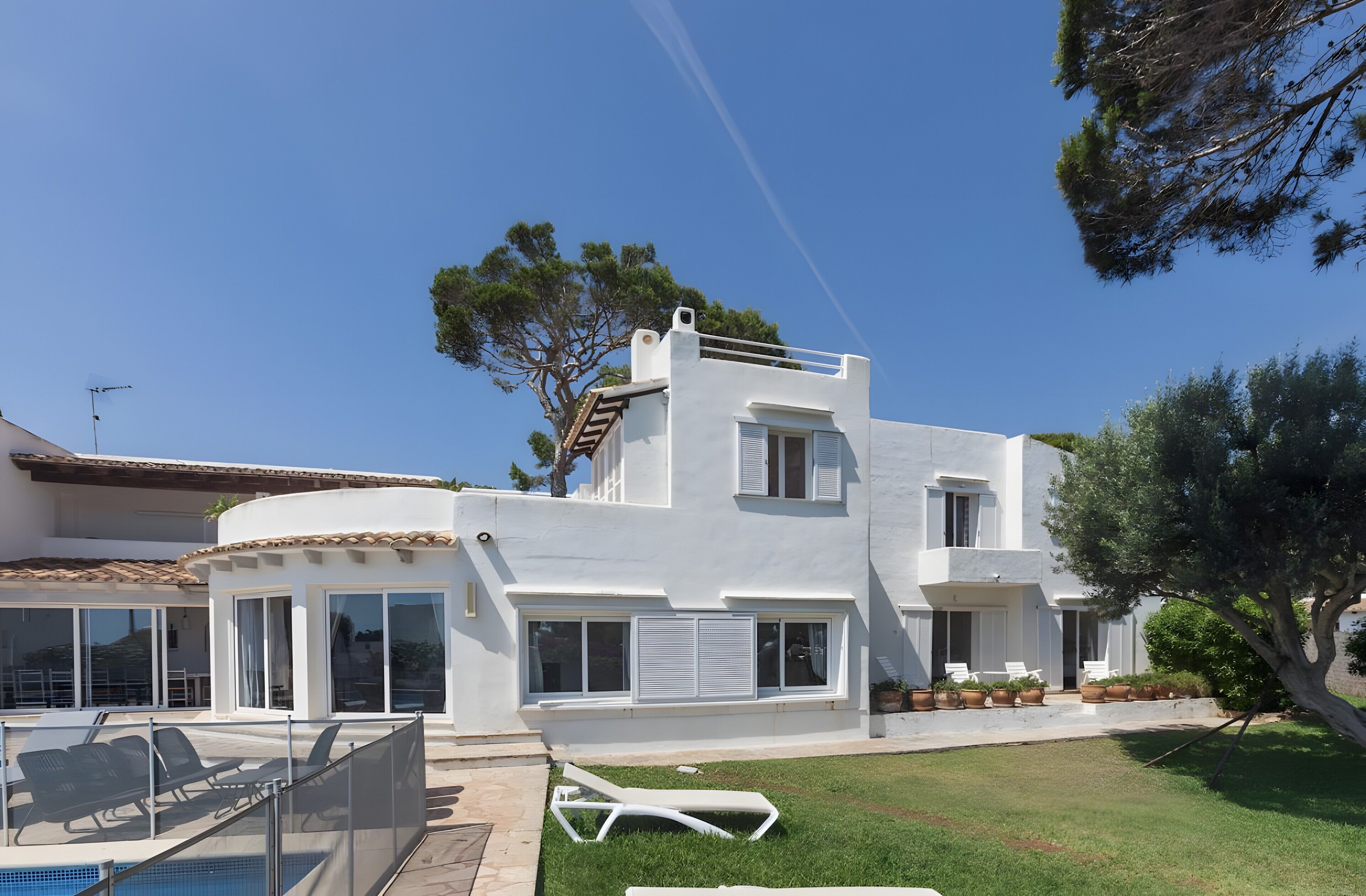 A modern two-story house with a swimming pool, outdoor seating, and a well-maintained lawn.