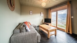 A living room with a sofa, a wooden coffee table, a flat-screen TV, and a large window with a mountain view. - Chalet 'Célestine 7 Bedrooms - Sauna' with Mountain View, Private Terrace and Wi-Fi (Verchaix)