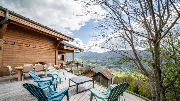 A wooden deck with outdoor furniture, a view of the landscape, and a building with a wooden exterior. - Chalet 'Célestine 7 Bedrooms - Sauna' with Mountain View, Private Terrace and Wi-Fi (Verchaix)