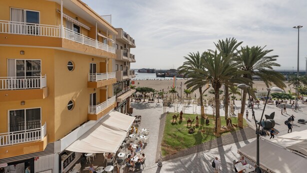 A multi-story hotel with balconies, outdoor seating, and a view of the beach.