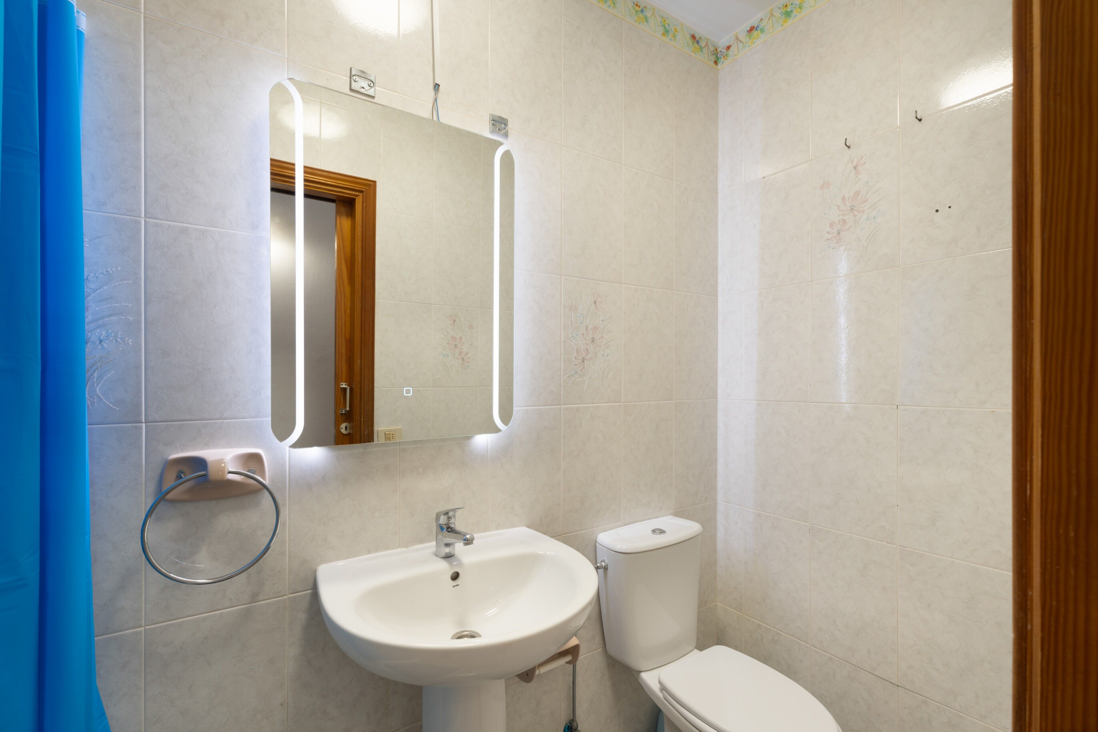 Een badkamer met een wastafel, spiegel, toilet en een blauw douchegordijn.