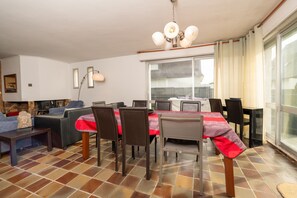 A dining area with a table set for four, surrounded by chairs, a sofa, and a television.
