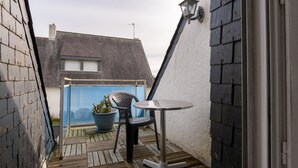 A small outdoor balcony with a table and chairs, a potted plant, and a view of a building with a sloped roof. - Holiday Home 'Maison Guidel Plage' with Sea View, Private Terrace and Wi-Fi (Guidel)