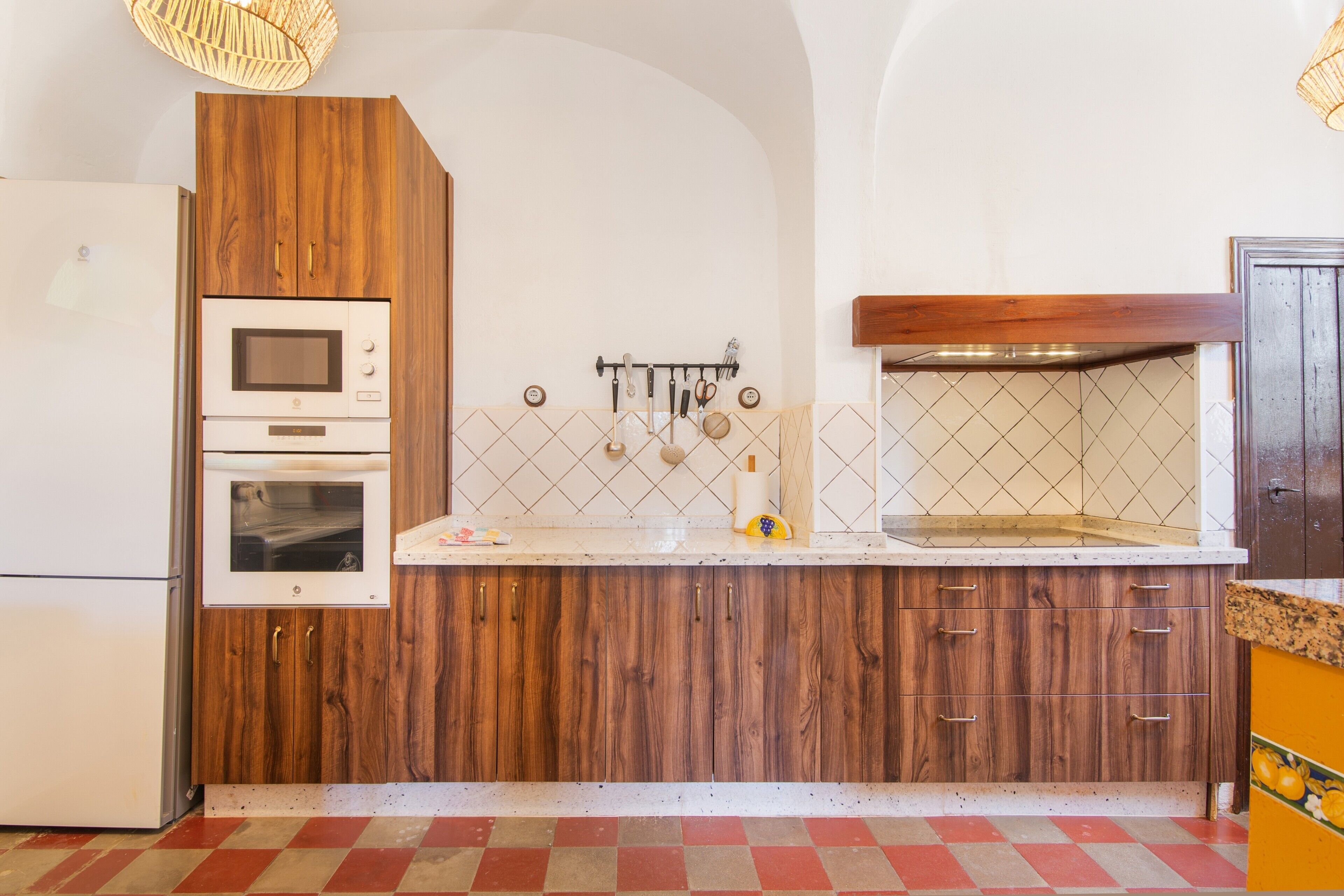 Een keuken met houten kastjes, een magnetron, oven en een hangrek.