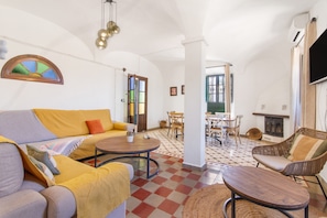 Una sala de estar con sofá, una mesa redonda de madera, una silla de mimbre, una chimenea y un comedor con sillas y una mesa.