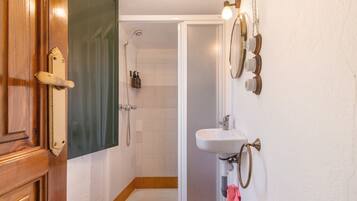 Ein Badezimmer mit Holztür, Dusche, Waschbecken und Handtuchhalter.
