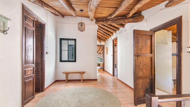 Un pasillo con puertas de madera, un banco, un tapete tejido y una lámpara colgante.
