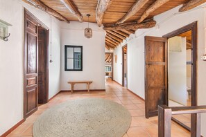 Un couloir avec des portes en bois, un banc, un tapis tissé et un luminaire suspendu.