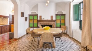 Un comedor con una mesa redonda, sillas de mimbre, un tazón amarillo, una chimenea de ladrillo y un suelo estampado.
