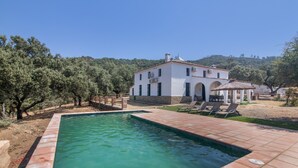 Una piscina con un edificio blanco al fondo, rodeada de árboles y un cielo despejado.
