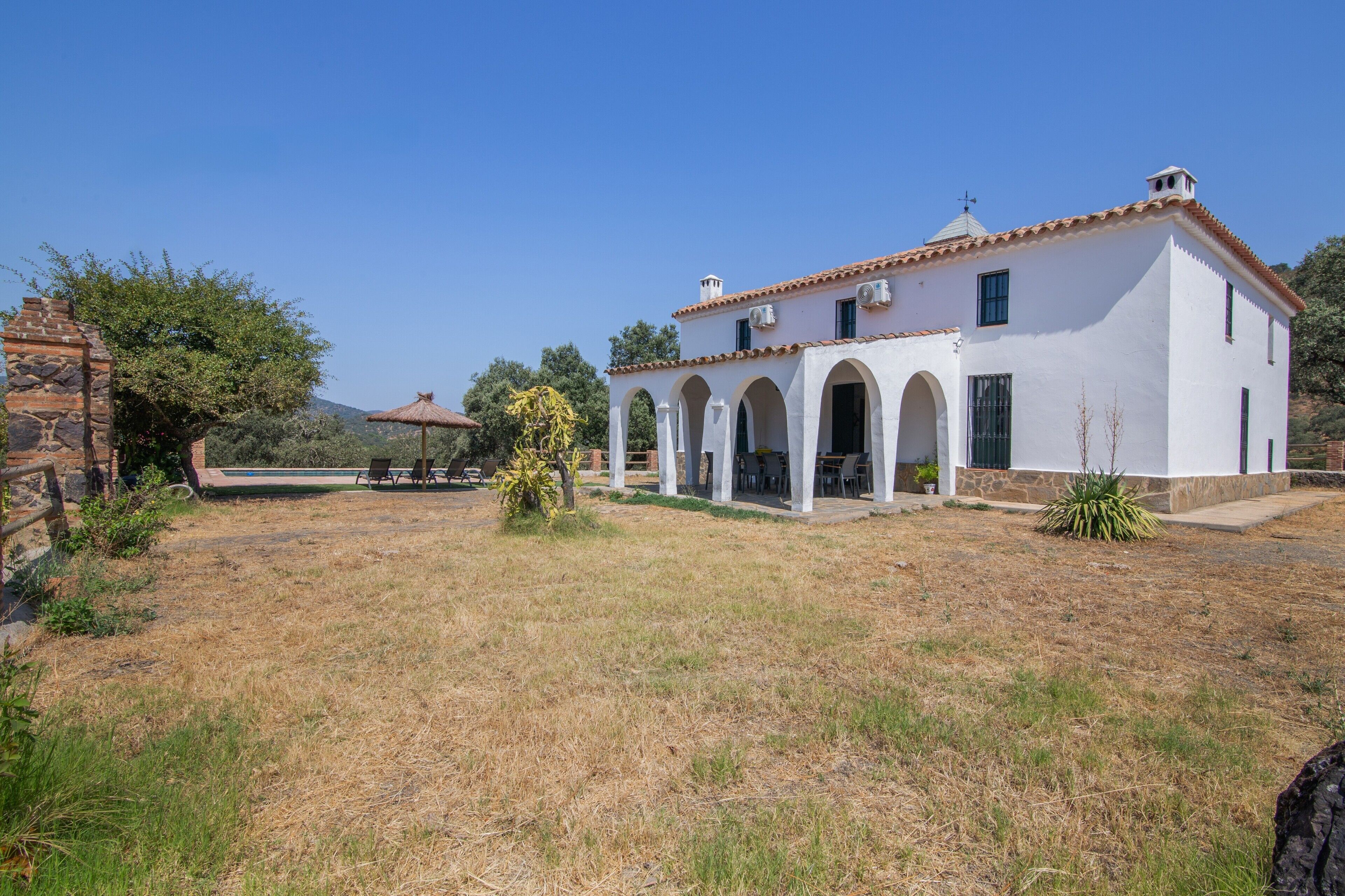 A white building with a tiled roof, arched windows, and a stone structure to the left.