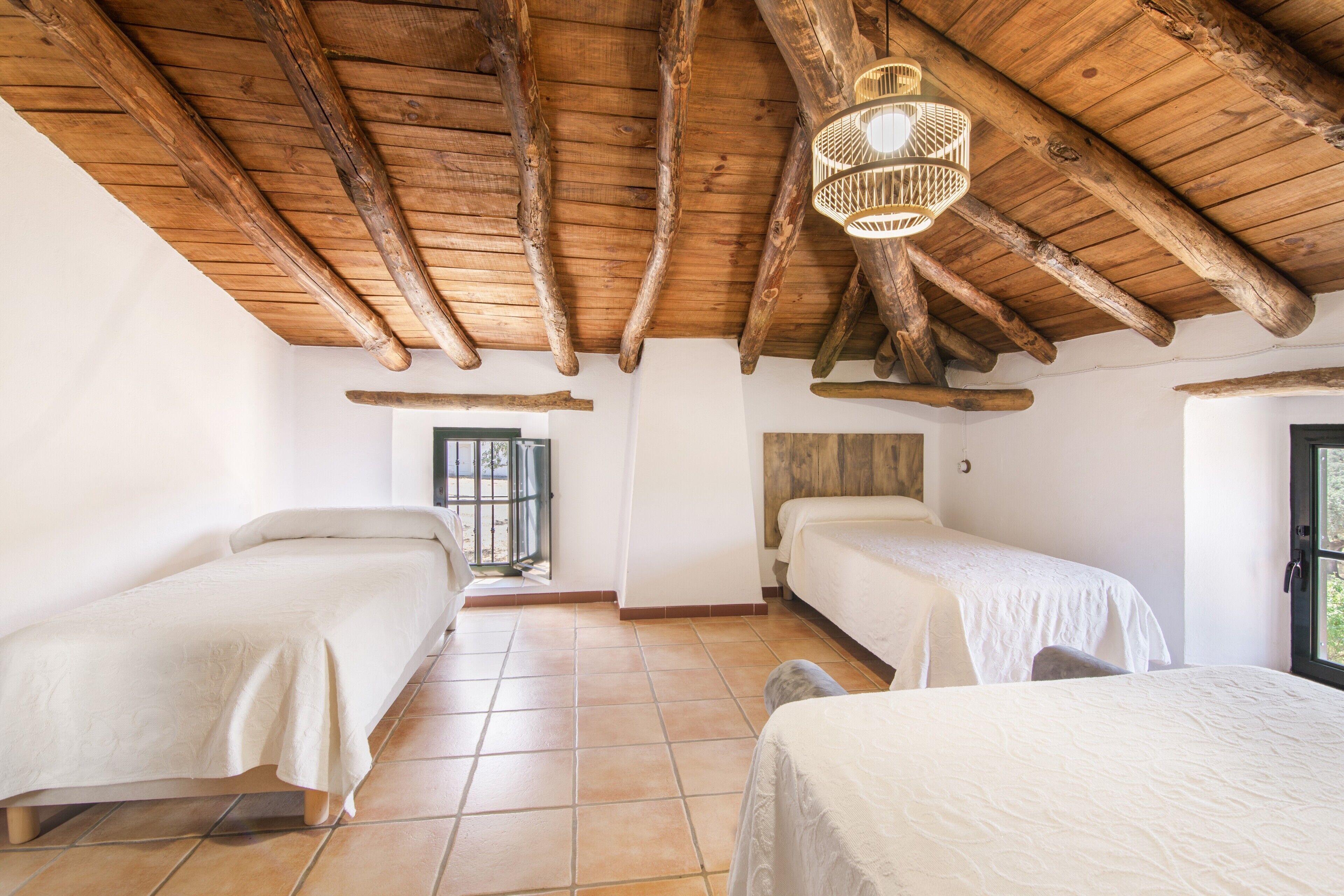 Una habitación con dos camas, vigas de madera en el techo, una lámpara de fibra y una ventana con vistas.