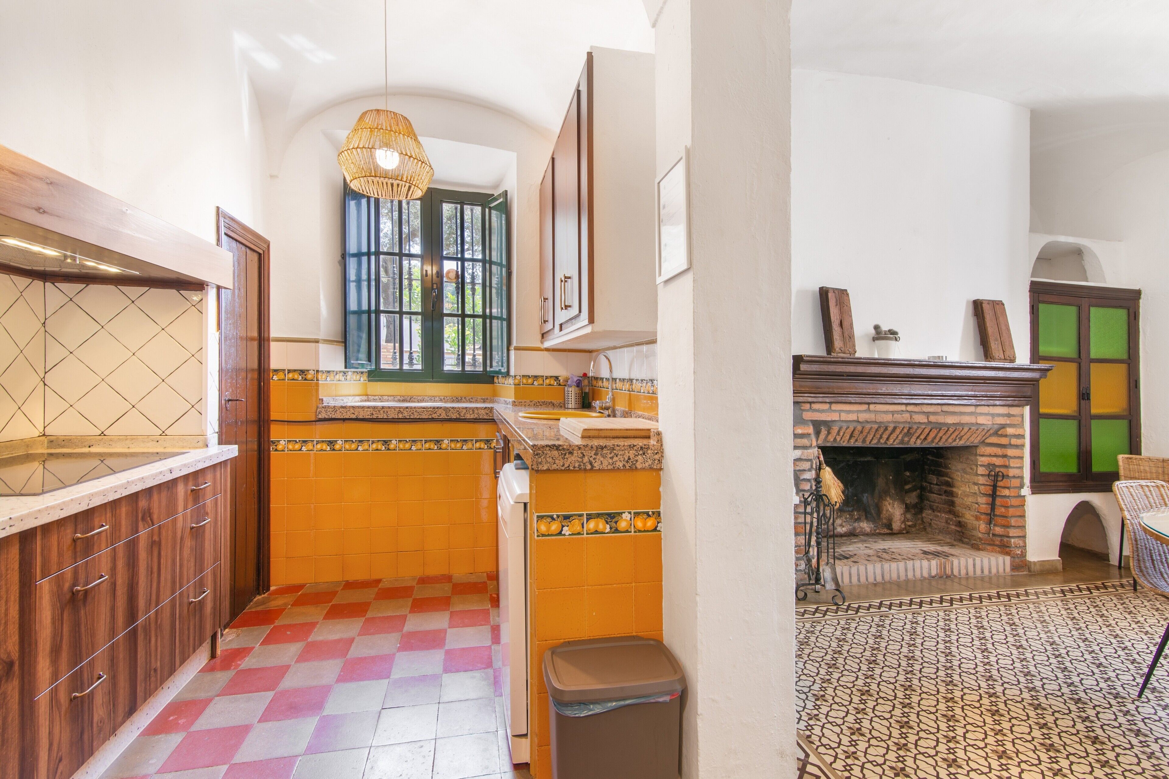A kitchen with a checkered floor, wooden cabinets, a window, and a fireplace.