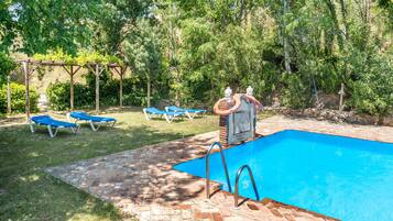 Une piscine entourée d’une terrasse en briques, de chaises longues bleues et d’une pergola couverte de plantes grimpantes.