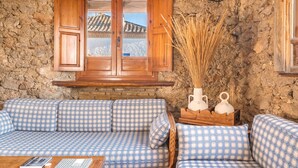 Ein rustikaler Raum mit einem karierten Sofa, einem Holzkasten mit geöffneten Türen und einer Steinwand.