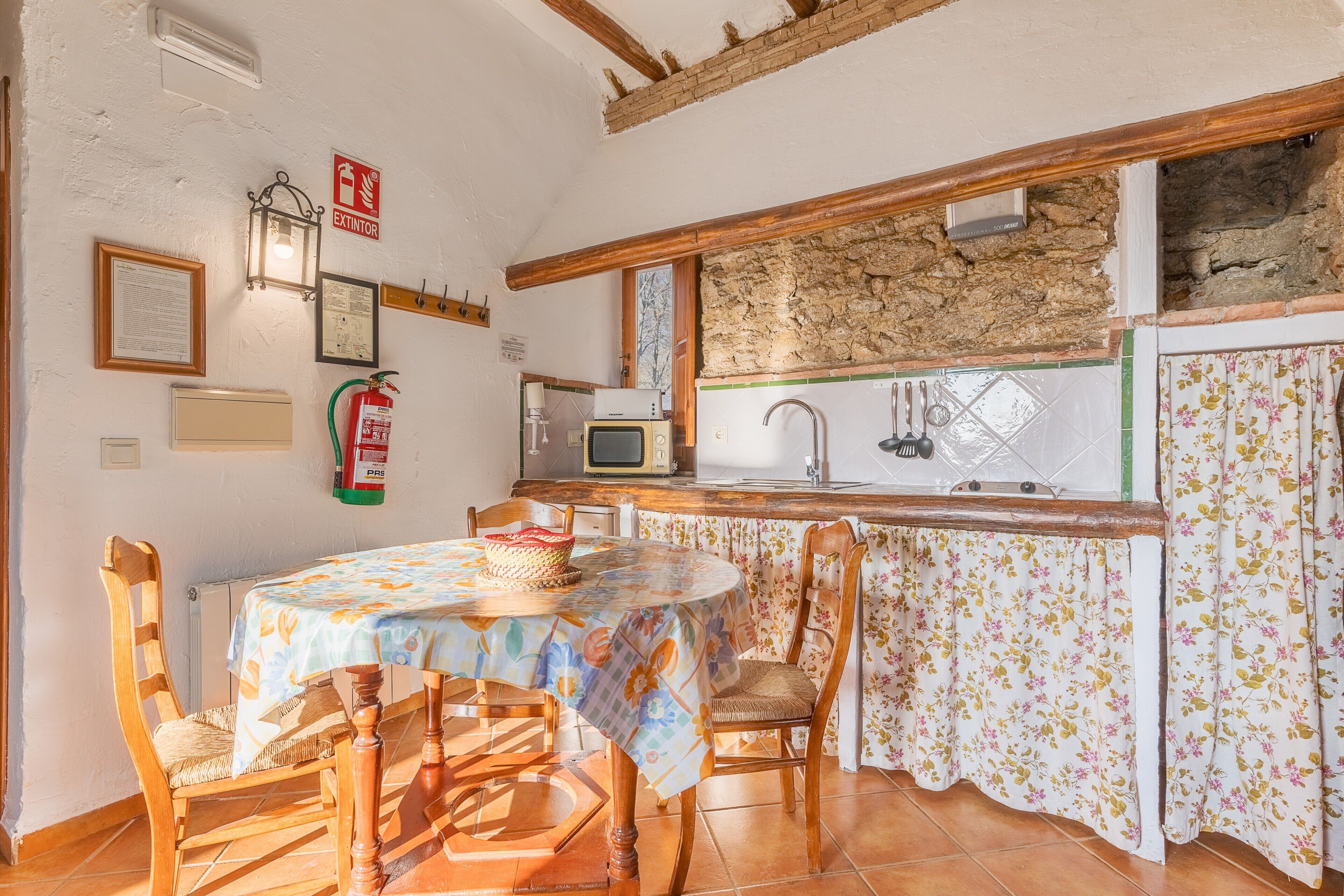 A kitchen with a stone wall, wooden beams, a table with chairs, a microwave, and a sink.